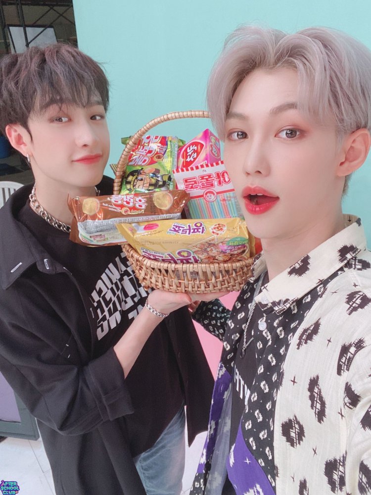 Bang Chan and Felix holding food behind blue background 